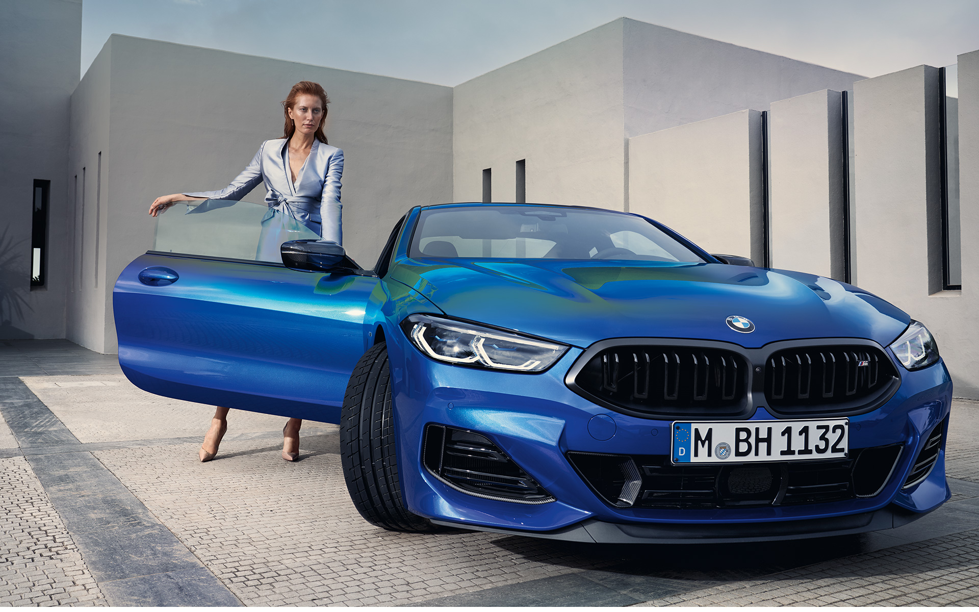 BMW M850i xDrive Coupé G15 LCI Facelift 2022 M Portimao Blue metallic sedd framifrån parkerad med kvinnlig modell i öppen passagerardörr